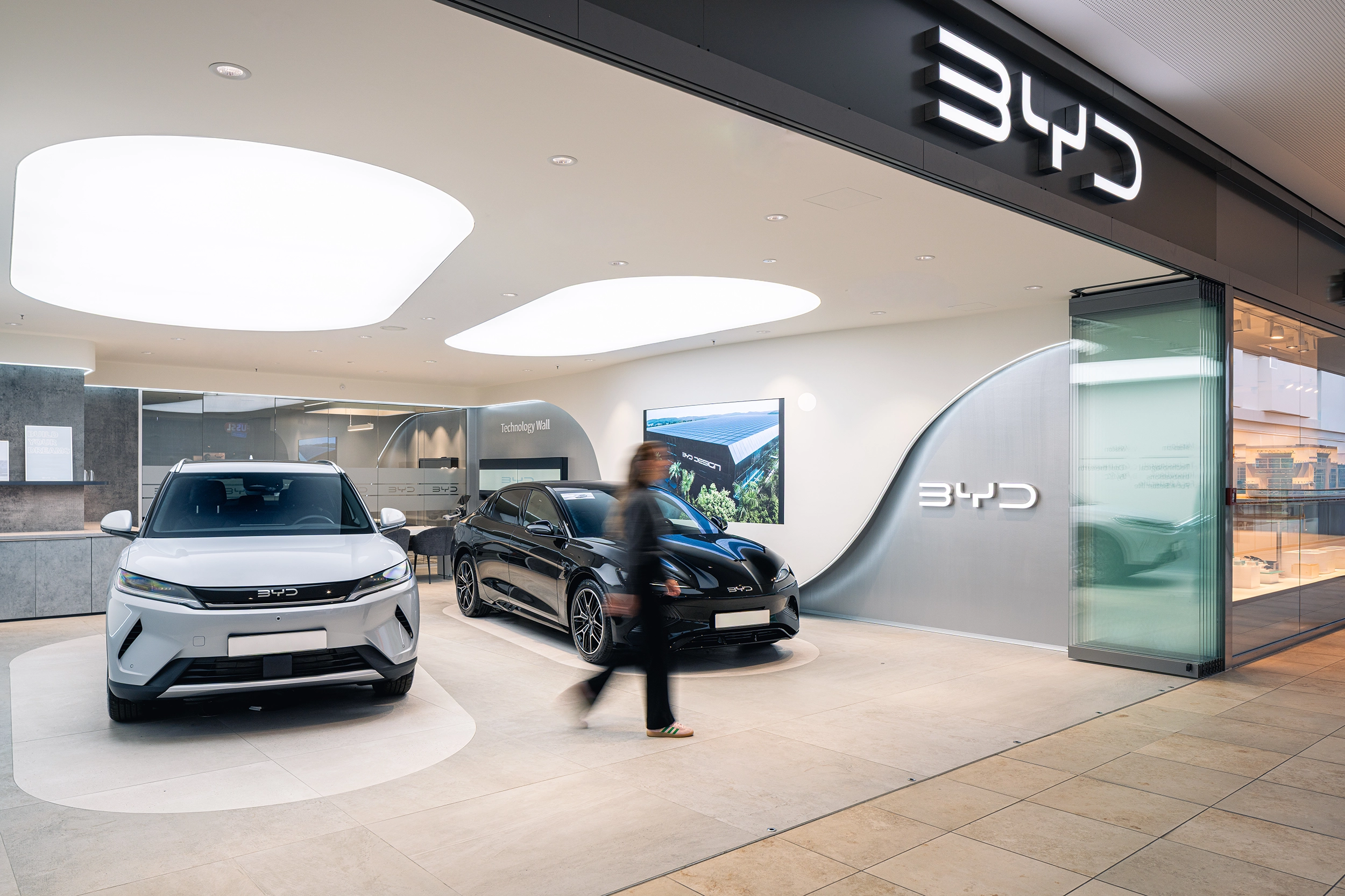 Wide view of a BYD car showroom with a white electric car and brand displays – automotive retail interior by Vizona