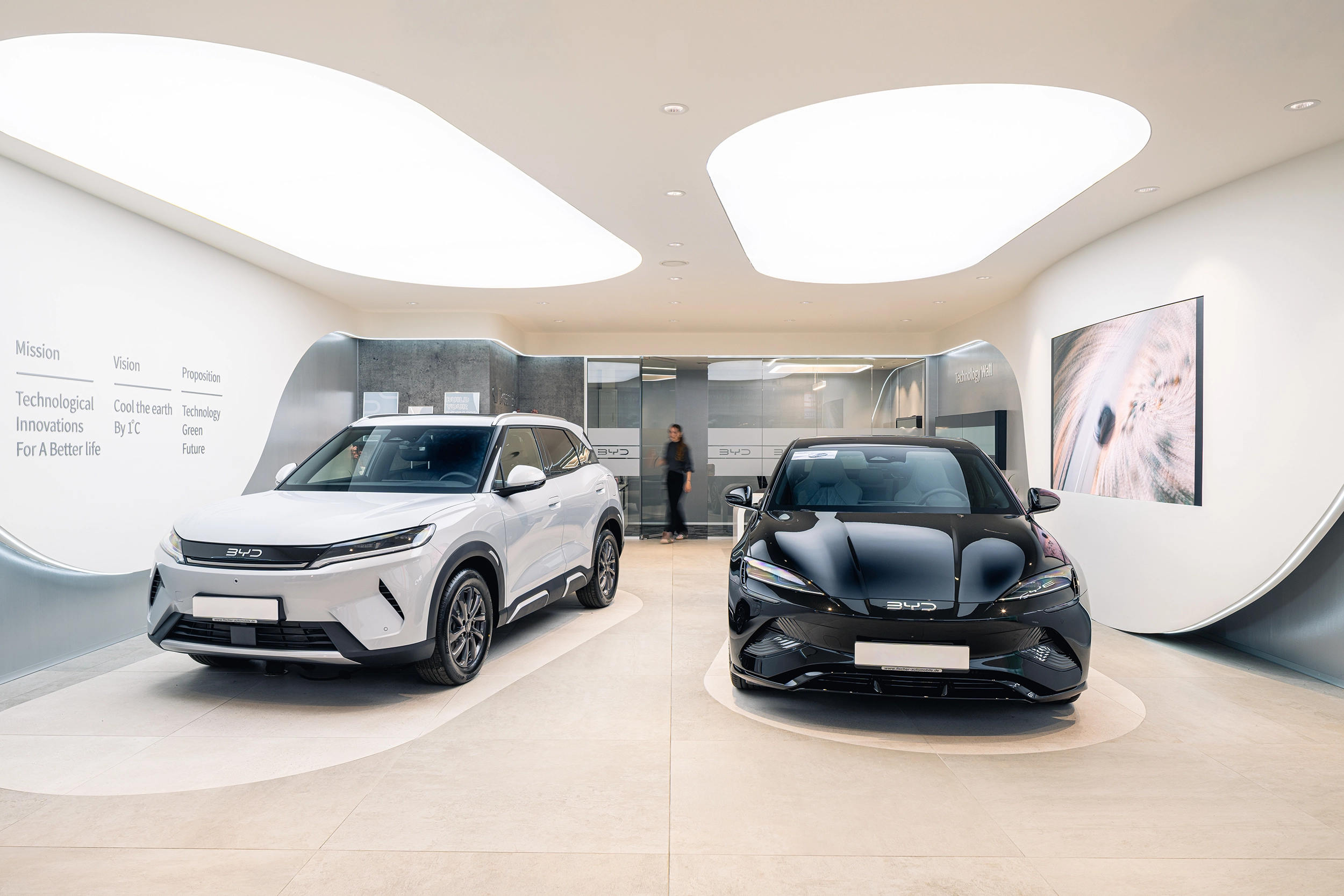 BYD dealership showroom with white and dark electric cars under curved ceiling lighting – car showroom design by Vizona