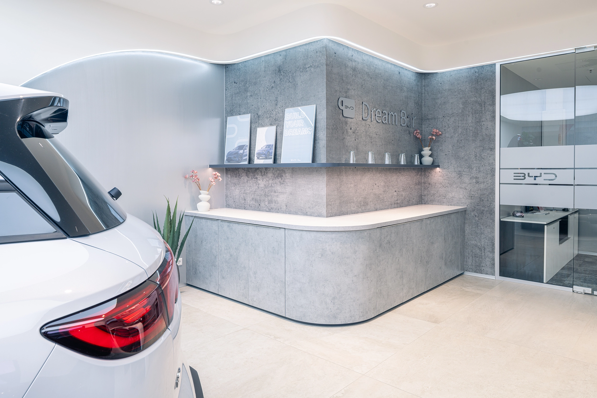 Reception area of a BYD car showroom with a concrete counter and white electric car – automotive retail design by Vizona